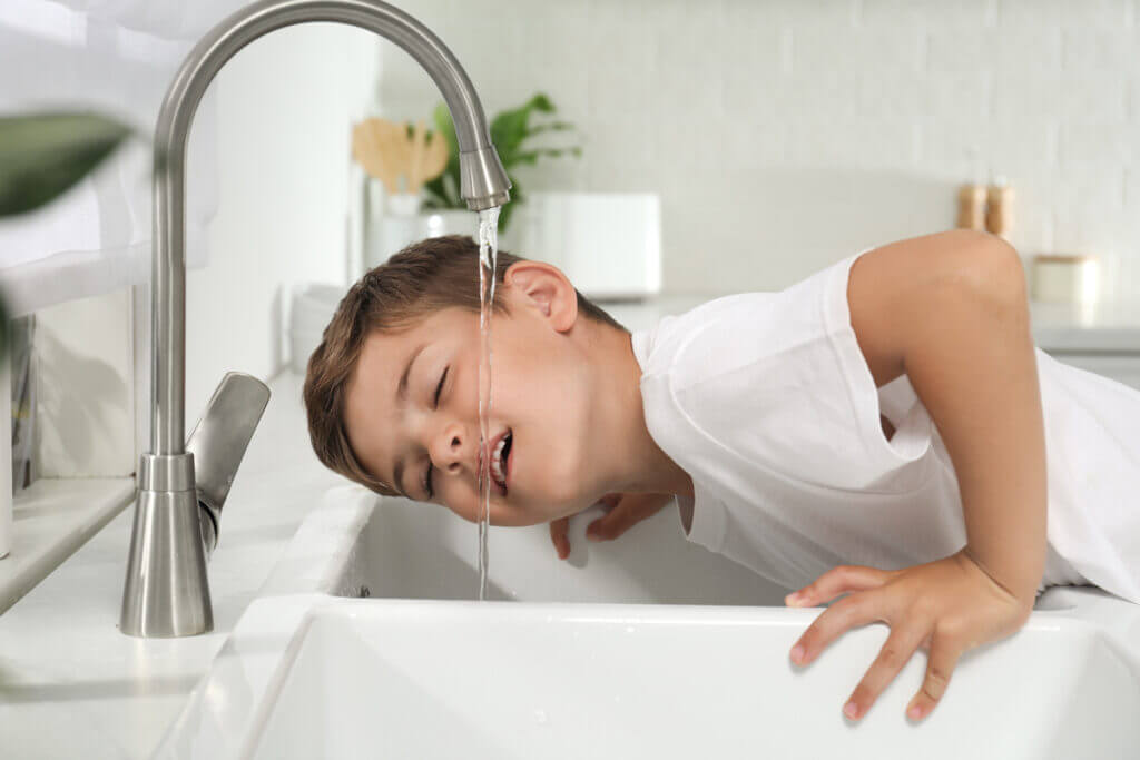 Kind trinkt gefiltertes Wasser direkt aus dem Wasserhahn mit eingebautem Wasserfilter im modernen Badezimmer