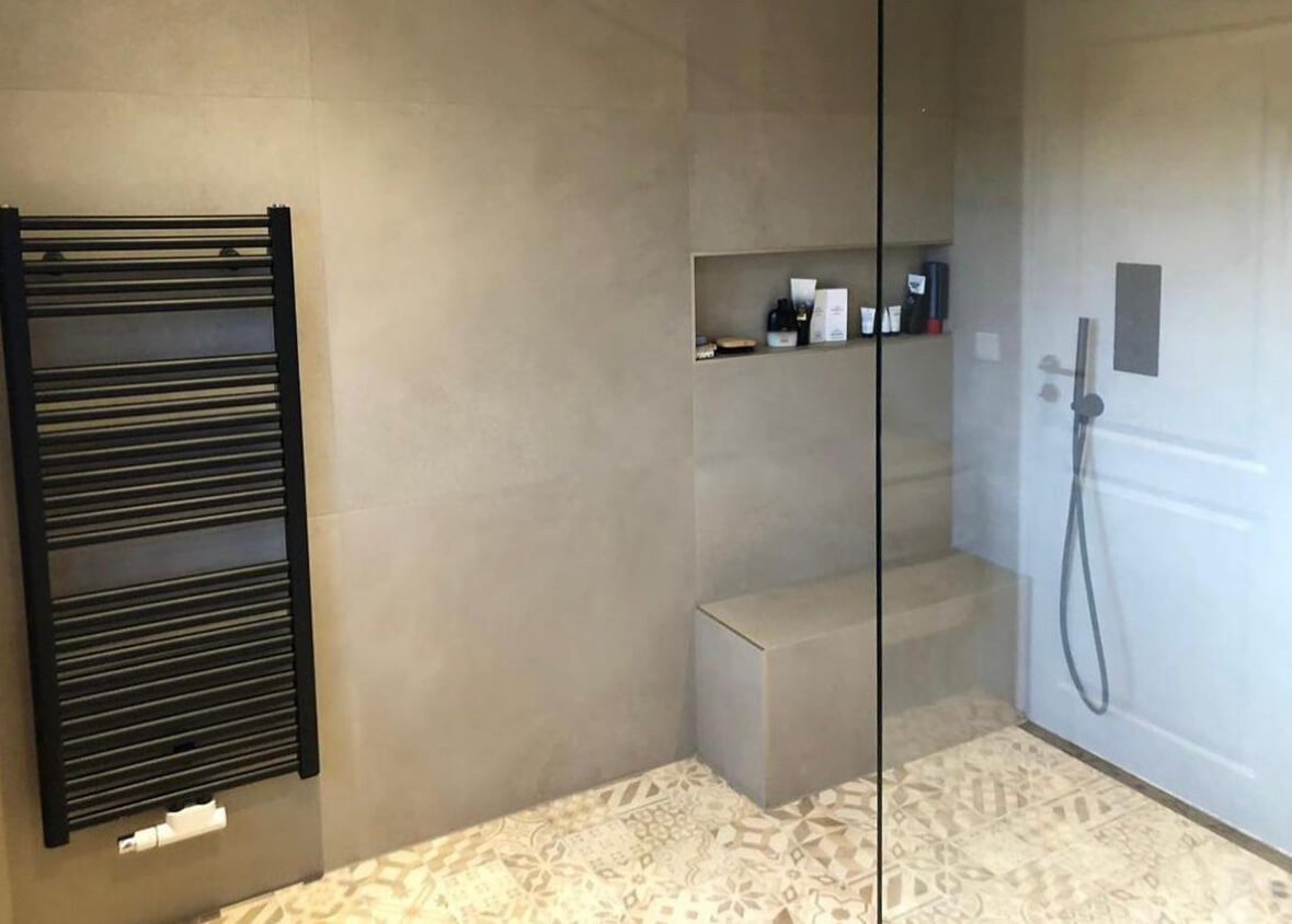 FAQ Badezimmermodernisierung - moderne begehbare Dusche mit Sitzbank, Handtuchheizkörper und Wandnische, häufig nachgefragte Badgestaltung im zeitlosen Design.